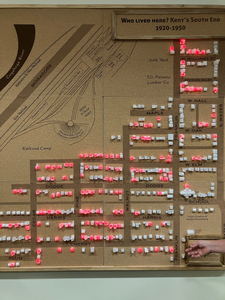 Images show a 60 inch by 60 inch map of a neighborhood with 350 transparent houses, some lit up to show positive responses to questions like "where did railroad workers live in 1920?" 